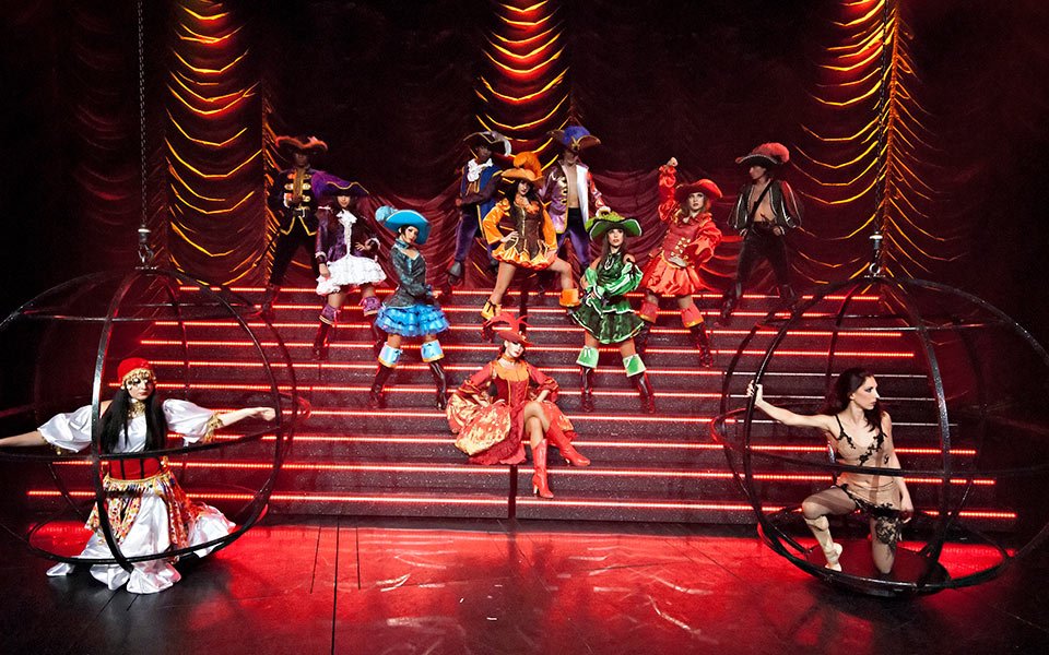 Colorful theatrical performance with dancers in vibrant costumes on a stage with dramatic lighting | MSC Cruises Colorful theatrical performance with dancers in vibrant costumes on a stage with dramatic lighting | MSC Cruises