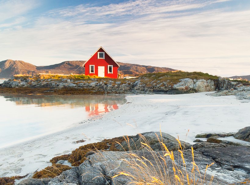 A red coastal cabin on a rocky shore with white sand and calm waters | MSC Cruises A red coastal cabin on a rocky shore with white sand and calm waters | MSC Cruises