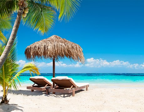 Two lounge chairs under a thatched umbrella on a tropical beach with turquoise water | MSC Cruises Two lounge chairs under a thatched umbrella on a tropical beach with turquoise water | MSC Cruises