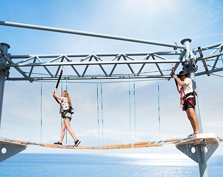 Guests enjoying a ropes course adventure over the ocean under a clear blue sky | MSC Cruises Guests enjoying a ropes course adventure over the ocean under a clear blue sky | MSC Cruises