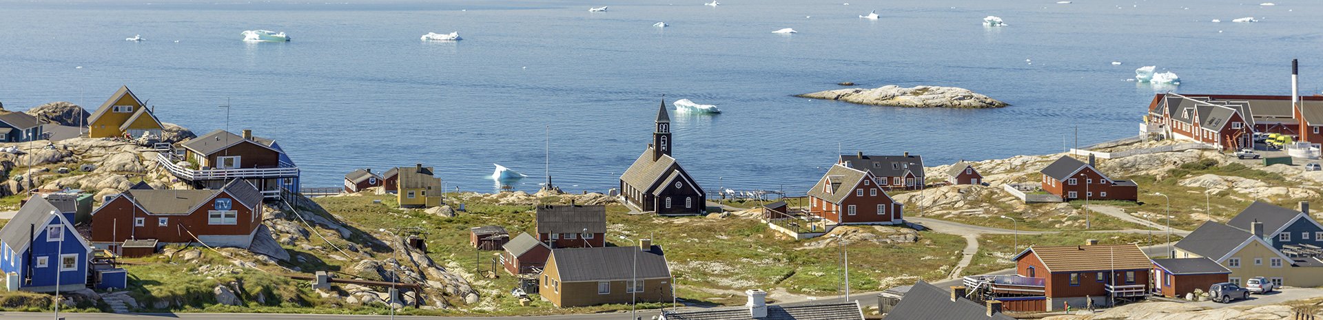 Colorful houses and a church overlooking an Arctic coastline with icebergs in the distance | MSC Cruises