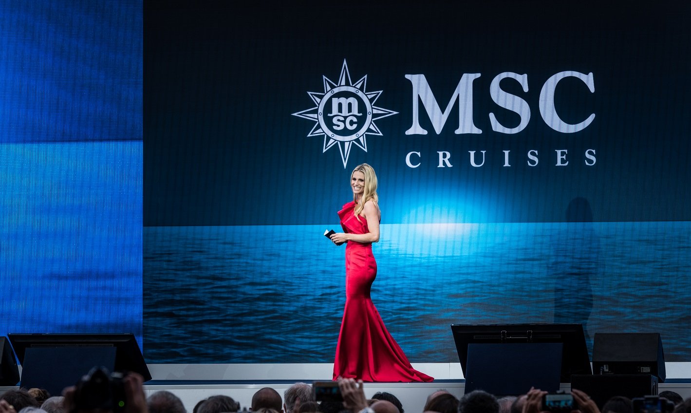 A woman in a red dress on stage with MSC Cruises branding and ocean backdrop | MSC Cruises