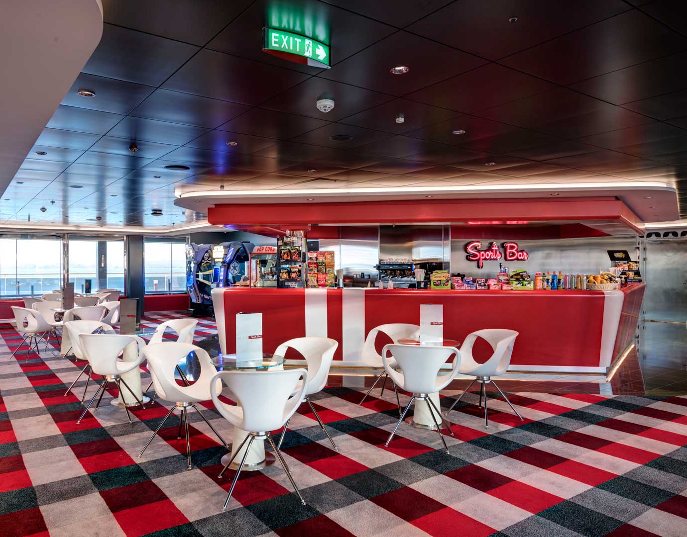 Modern sports bar with red decor, white chairs, and arcade games onboard a cruise ship | MSC Cruises