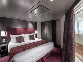 Luxurious cruise cabin with king-size bed and private balcony overlooking the ocean | MSC Cruises