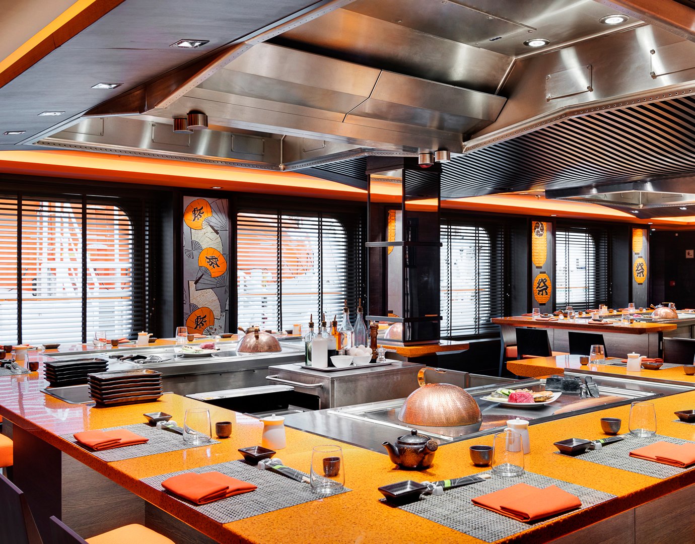 Teppanyaki-style dining area with vibrant orange decor and table settings onboard | MSC Cruises Teppanyaki-style dining area with vibrant orange decor and table settings onboard | MSC Cruises